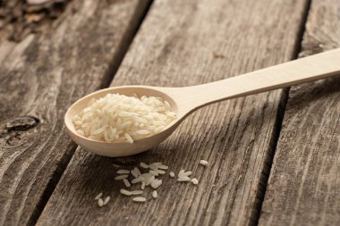 Tahta bir kaşık ve çiğ beyaz pirinç, gün ışığında ahşap bir masada.