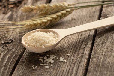 Tahta bir kaşık ve çiğ beyaz pirinç, gün ışığında ahşap bir masada.
