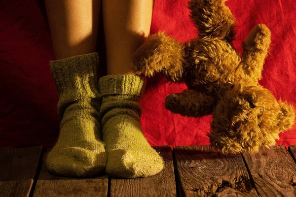 female feet on the floor next to a teddy bear in the dark with a night lamp