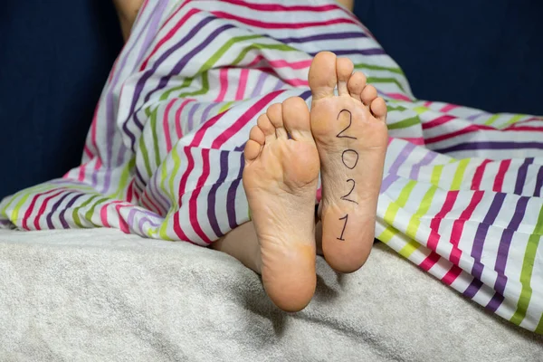 2021 written on the female foot of a girl lying on the bed at home in the bedroom