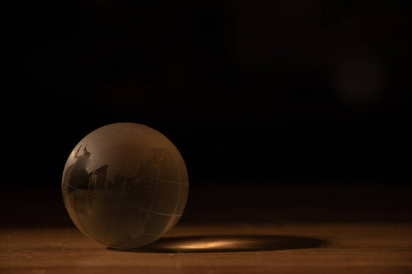 стеклянный прозрачный земной шар лежит на деревянном столе в темноте