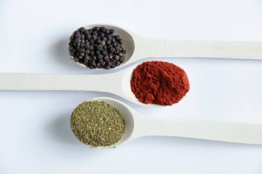 Farklı baharat ve biber çeşitlerine sahip ahşap kaşıklar izole bir arka planda yakın plan.