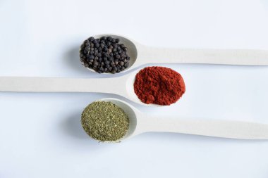 Farklı baharat ve biber çeşitlerine sahip ahşap kaşıklar izole bir arka planda yakın plan.