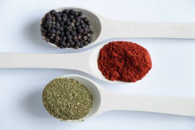 Farklı baharat ve biber çeşitlerine sahip ahşap kaşıklar izole bir arka planda yakın plan.