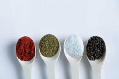 Farklı baharat ve biber çeşitlerine sahip ahşap kaşıklar izole bir arka planda yakın plan.