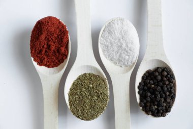 Farklı baharat ve biber çeşitlerine sahip ahşap kaşıklar izole bir arka planda yakın plan.