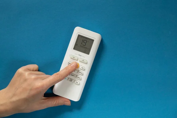 stock image female hand switches button on white remote control of air conditioner on isolated background