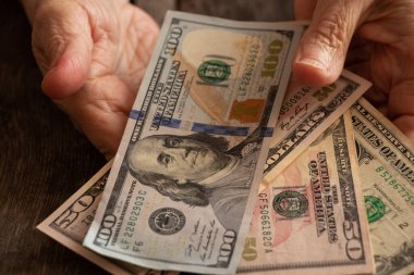 Amerikan doları üzerinde yaşlı bir kadının elleri ahşap bir masanın üzerinde.