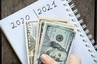 2020 ve 2021 yıllarında iki sütunlu bir defter tahtadan arka planda bir kızın elinde bir tomar Amerikan doları, yılın mali sonuçları.