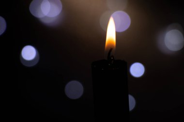 Karanlıktaki mum alevi bulanık çelenklerin arkasında Bokeh, din