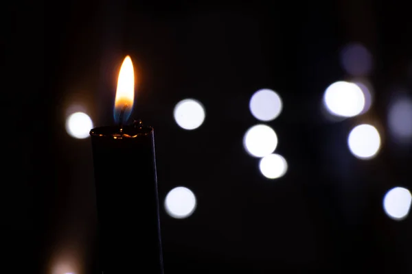 candle flame in the dark on the background of blurry garlands bokeh, religion