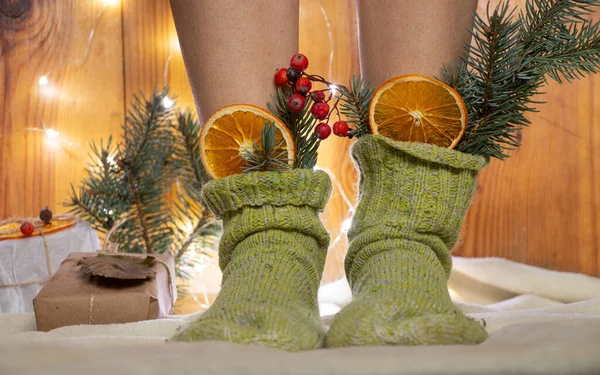 girl at home in green socks with an orange and a branch of a Christmas tree inside on a white carpet on the floor waiting for the new year.