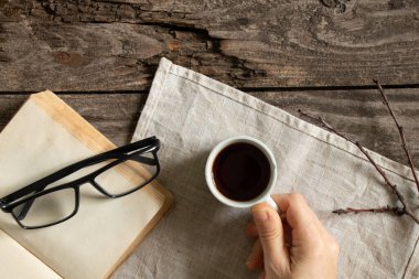 Bir kadının eli, sabahları bir kitabın yanında bir fincan kahve tutar. Bir peçetenin üzerinde, tahta bir masanın üzerinde, bardakların yanında.