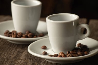 İki beyaz fincan ve kahve tanecikli bir fincan tabağı sabah mutfakta, ahşap bir masanın üzerinde.