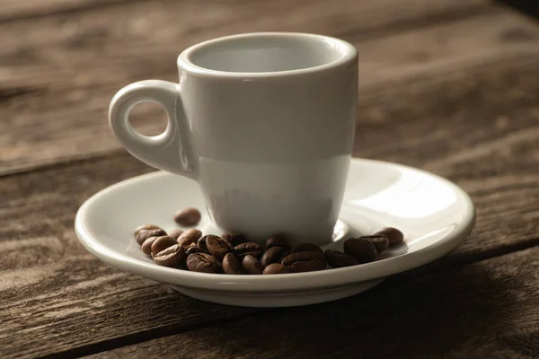 白いカップとコーヒーの粒が入ったソーサーがキッチンの木のテーブルの上に立っています — ストック写真