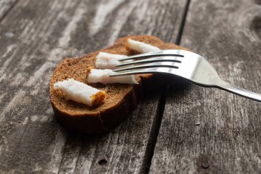 Domuz pastırmalı bir parça siyah ekmek ve öğle yemeği için ahşap bir masada çatal.