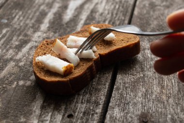 Domuz pastırmalı bir parça siyah ekmek ve öğle yemeği için ahşap bir masada çatal.