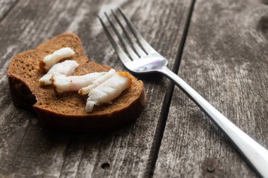 Domuz pastırmalı bir parça siyah ekmek ve öğle yemeği için ahşap bir masada çatal.