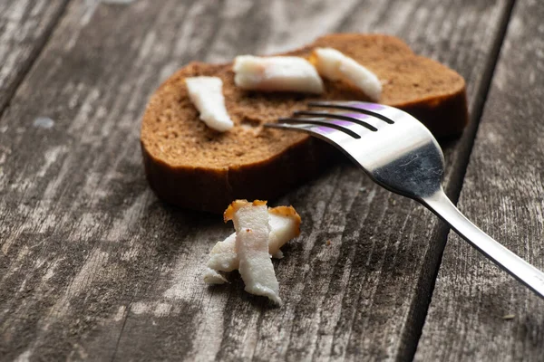 Domuz pastırmalı bir parça siyah ekmek ve öğle yemeği için ahşap bir masada çatal.