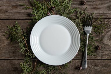 Beyaz tabak ve çatal dalların üzerinde bir Noel ağacı ile birlikte ahşap bir masanın üzerinde duruyor, Yeni Yıl dekoru.