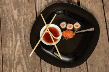 Kırmızı havyar, kırmızı balıklı suşi kaşığı ve soya sosu. Mutfaktaki masada duran siyah tabakta.