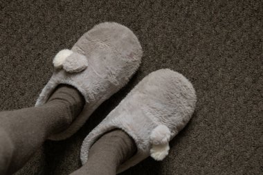 Sıcak tayt giymiş bir kızın bacakları ve evdeki gri halıda gri yumuşak terlikler, tepeden tırnağa manzara.