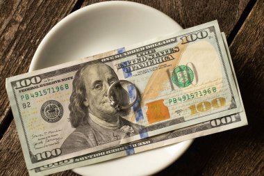 100 dolar ve ahşap arka planda sütyenleri olan beyaz altın bir yüzükleri var.