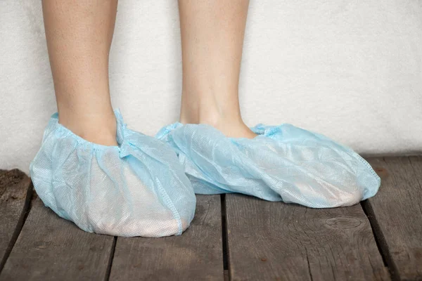 female legs in blue medical protective plastic shoe covers in hospital