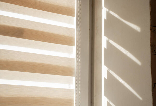 beige roller blinds day night on the window in the daytime in the sun close-up