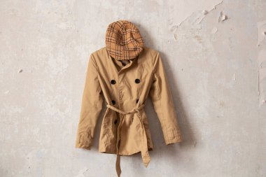 Evdeki beyaz bir duvarda asılı şık kadınların kahverengi yağmurlukları ve ekose şapkaları.