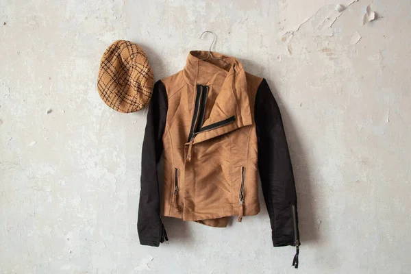 a brown women\'s jacket and a plaid cap hang on a white wall at home