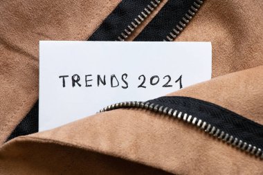 Inscription on a sheet of white paper trends 2021 in the pocket of a brown zipped jacket clipart