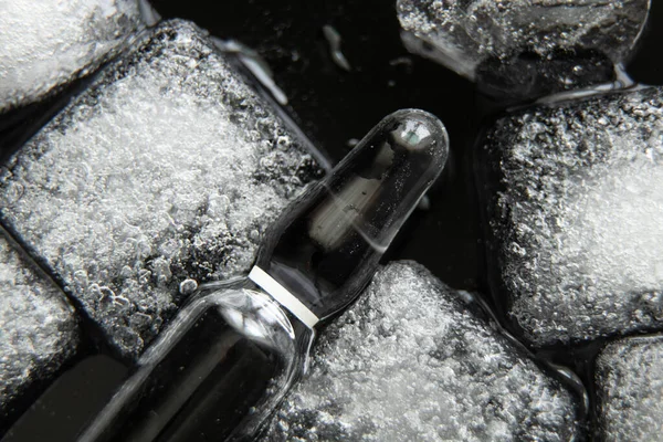 vaccine ampoule lies in ice on a black background close-up, vaccination