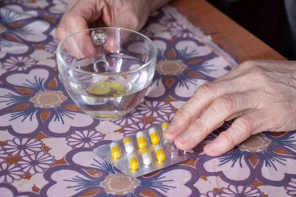 Elderly woman\'s hands hold medicine and next to water at the table, treatment