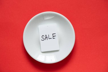 İndirimli beyaz fiyat etiketi, izole edilmiş kırmızı zemin üzerinde beyaz bir plaka üzerinde bulunur.