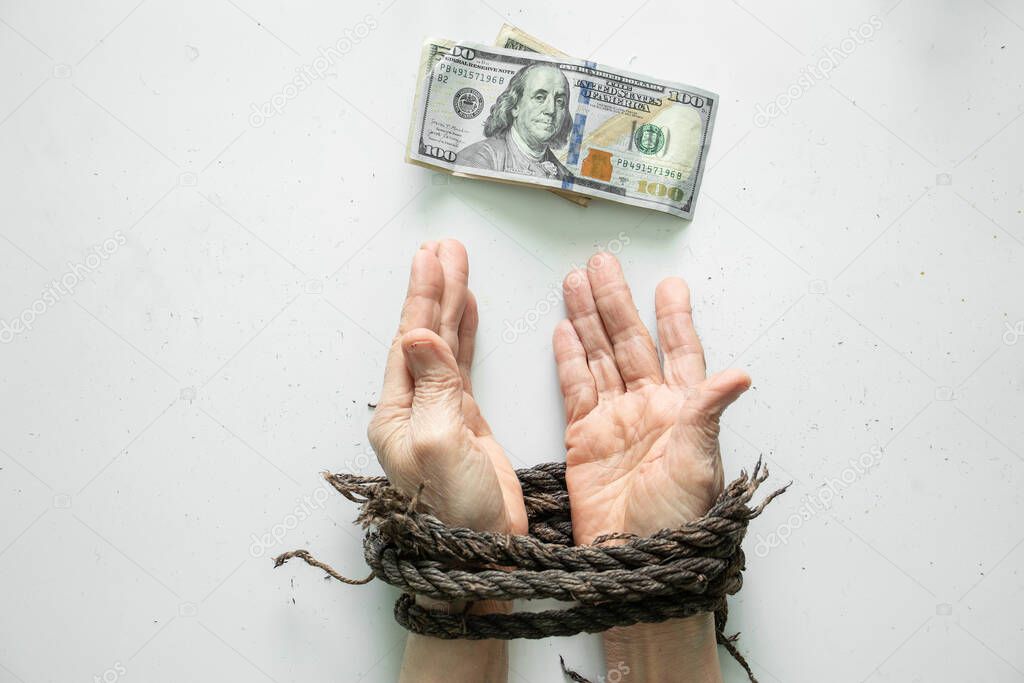 female hands tied with a rope and lie next to american dollars on a white background