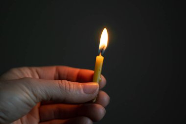 Karanlıkta yanan bir mum tutan kadın eli, mum alevi.
