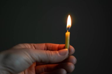 Karanlıkta yanan bir mum tutan kadın eli, mum alevi.