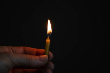 Karanlıkta yanan bir mum tutan kadın eli, mum alevi.