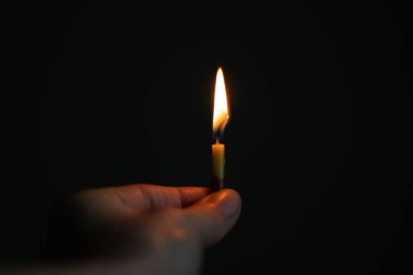 Karanlıkta yanan bir mum tutan kadın eli, mum alevi.