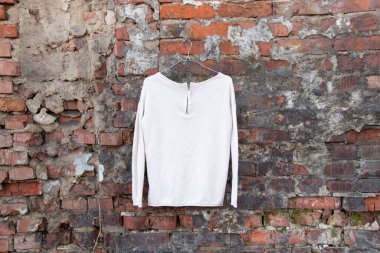 Açık renk süveter, sokaktaki tuğla bir duvarda asılı duruyor, moda kadın kıyafetleri.