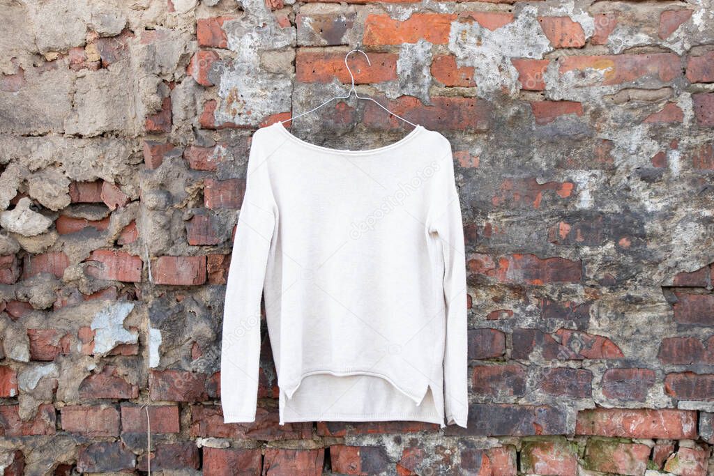 light sweater sweater hangs on a hanger on a brick wall on the street, fashion women's clothing