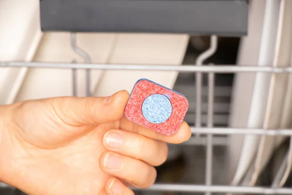 female hand holds a tablet for washing dishes for the dishwasher on the background of dirty plates, dishwasher, washing dishes