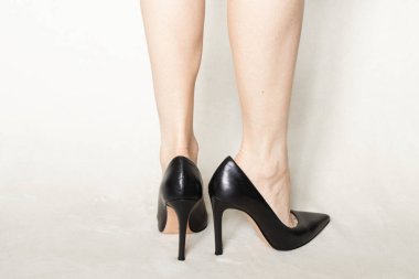 Siyah parmaklı, yüksek topuklu ayakkabılı genç kız evdeki beyaz halıda duruyor.