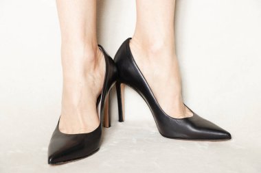 Siyah parmaklı, yüksek topuklu ayakkabılı genç kız evdeki beyaz halıda duruyor.