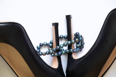 Beyaz arka planda siyah deri kadın ayakkabıları ve inci boncuklar, güzellik ve moda