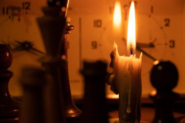 Satranç taşları satranç tahtasının ve saatin üzerinde durur ve karanlıkta yanan bir mumun yanında satranç oynar.