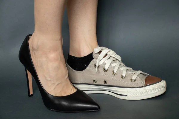 on one leg black high-heeled shoes on the other sport sneaker on the legs of a girl on an isolated dark blue background