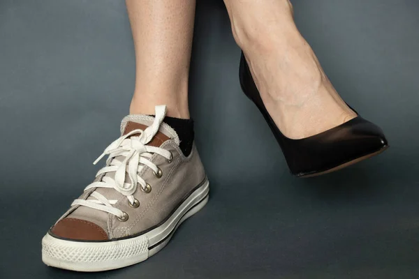 on one leg black high-heeled shoes on the other sport sneaker on the legs of a girl on an isolated dark blue background