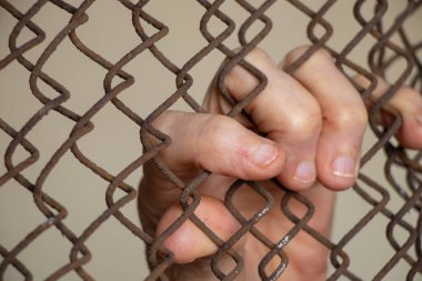 Yaşlı kadın elleri kilitte demirden yapılmış bir çite tutunuyor.